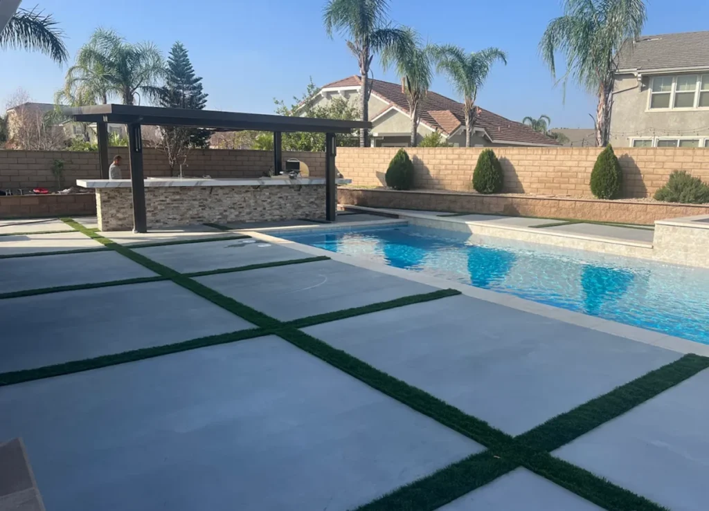 Rectangular backyard pool with concrete deck, artificial turf accents, and covered outdoor kitchen